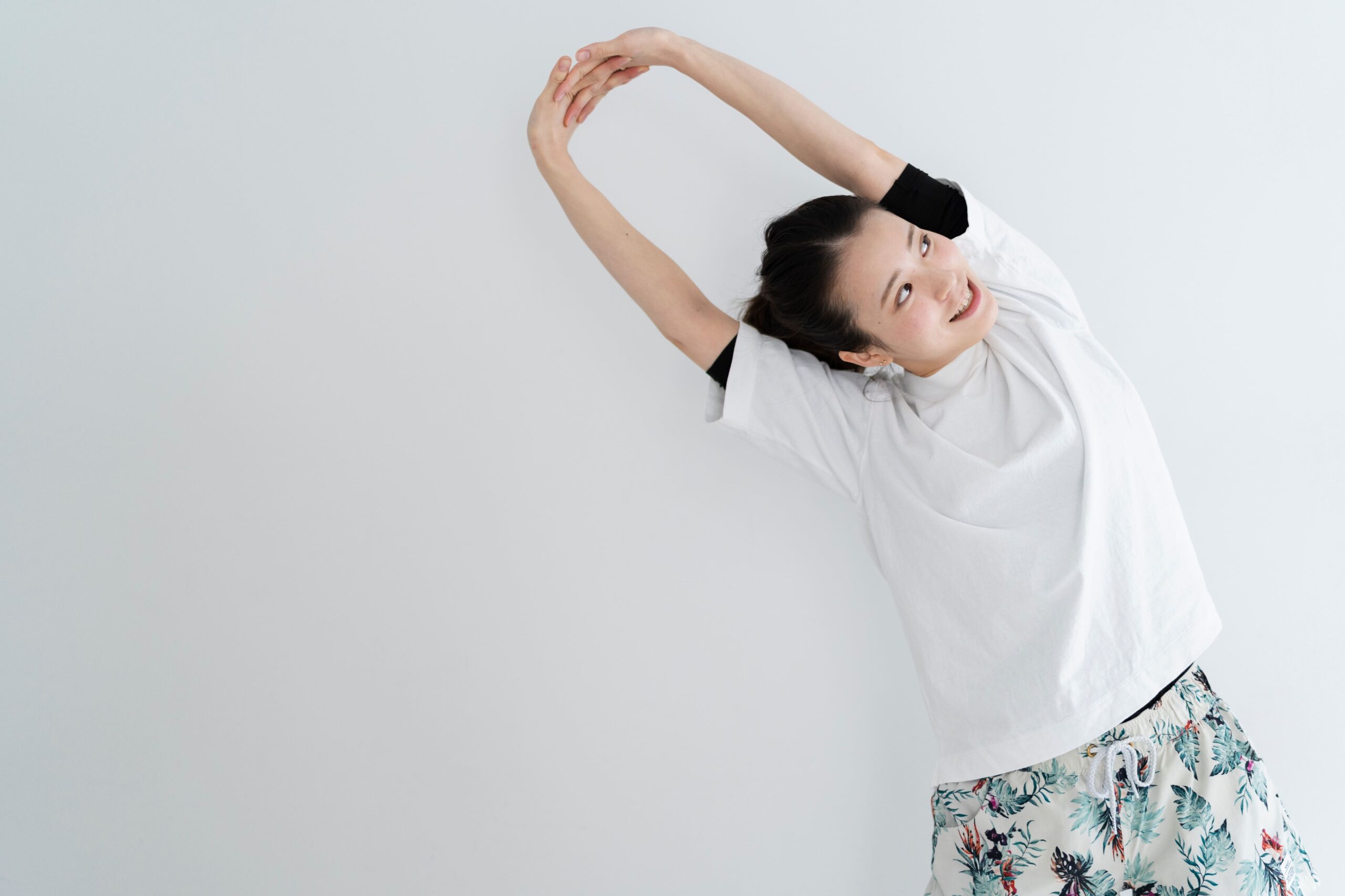 両腕を頭上に上げ、体を横へ傾けて肩と体側を伸ばす人物のイメージ写真