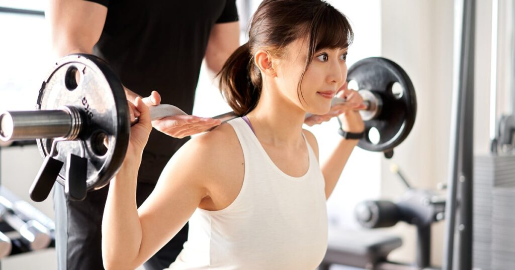 パーソナルトレーナーの補助を受けてスクワットする女性のイメージ