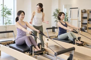 木製リフォーマーで座位のストラップ運動を教わる30〜40代の女性たちの生成イメージ（架空の日本人モデル・実店舗や実際のスタッフの写真ではありません）
